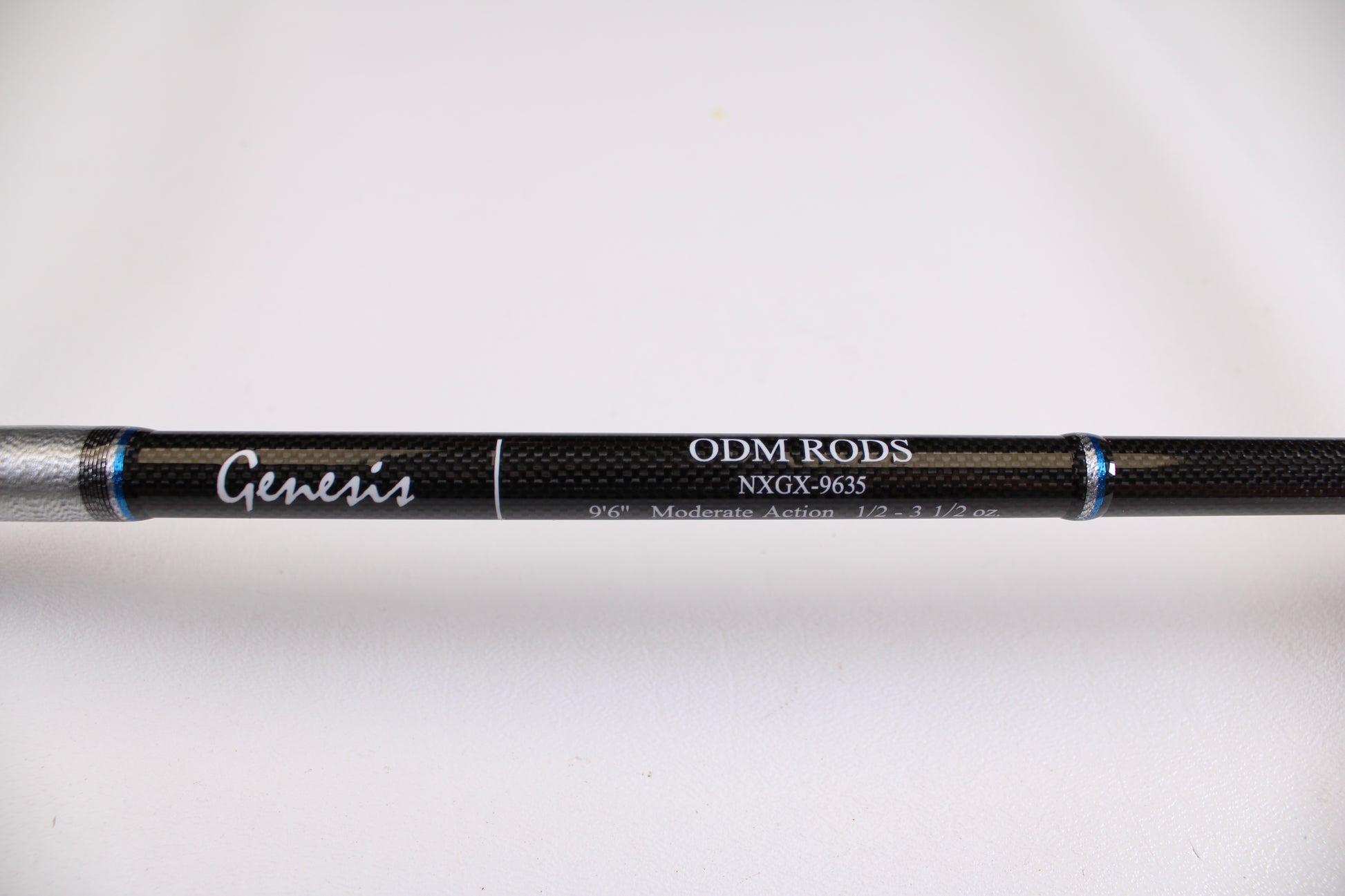 A close-up of an ODM Rods Genesis Surf NGX-9635 9'6" 2 Piece Used Spinning Rod in excellent condition, showing its black finish with silver and blue accents. Eligible for rod and reel trade-in—earn store credit on your next purchase.