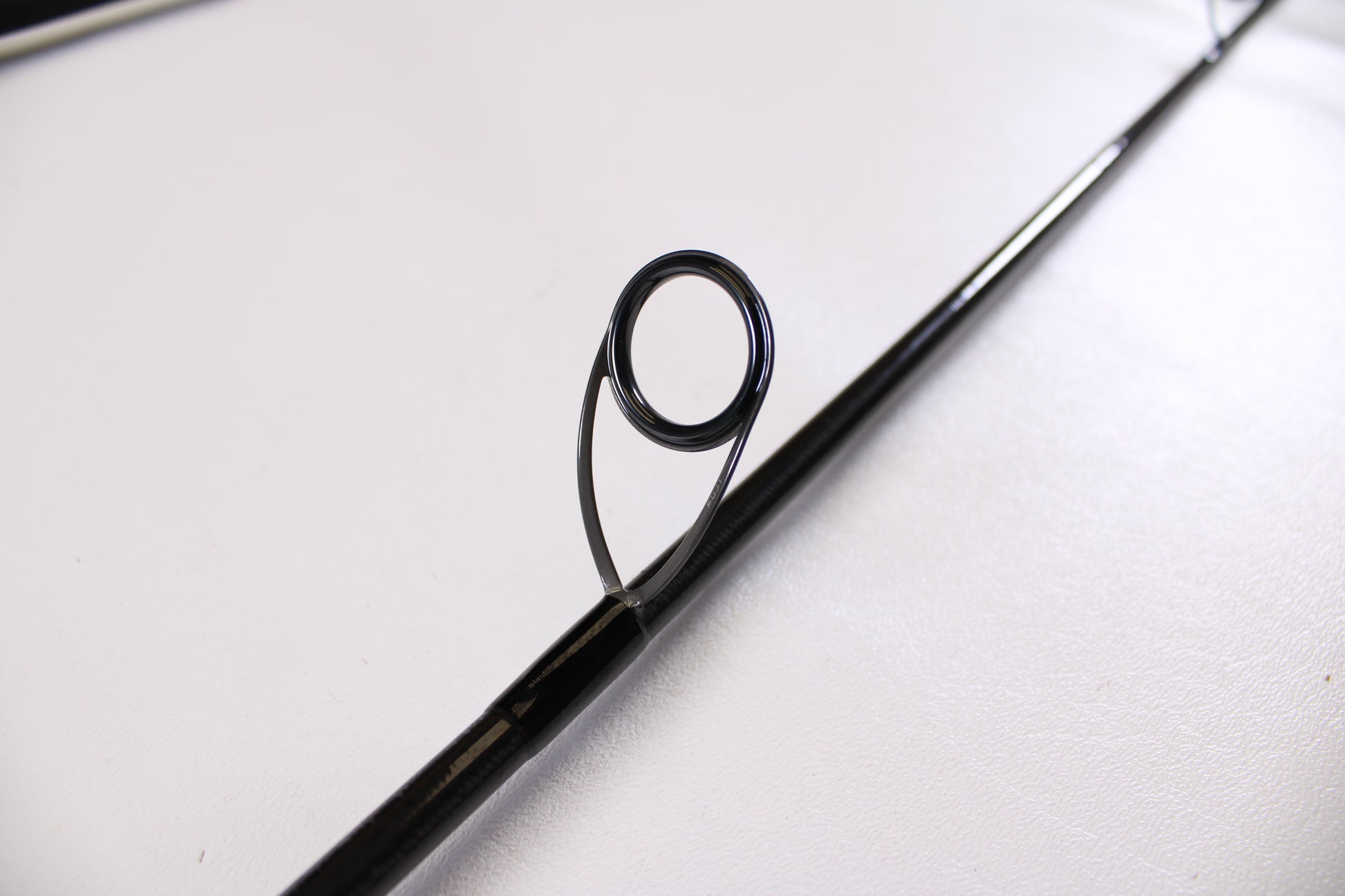 Close-up of an ODM Rods Genesis Surf NGX-802 8'0" used spinning rod guide on a white surface—excellent condition. Trade in your used gear like this through our Rod and Reel Trade-In Program for store credit.