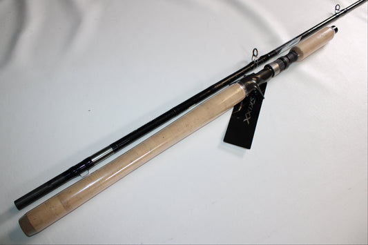 The Shimano SKIXX SKC86XH Used Casting Rod, in mint condition, features a cork handle and black shaft. Shown diagonally on a white surface, it has a black tag attached near the reel seat.
