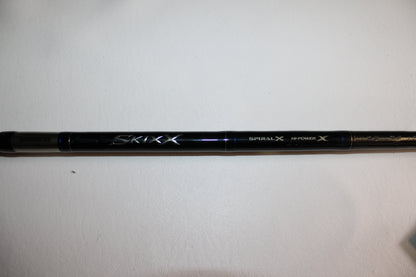 A close-up of the Shimano SKIXX SKC86XH Used Casting Rod in mint condition, showing "Shimano," "SKIXX," "Spiral X," and "Hi-Power X" on the black rod, placed on a white surface.