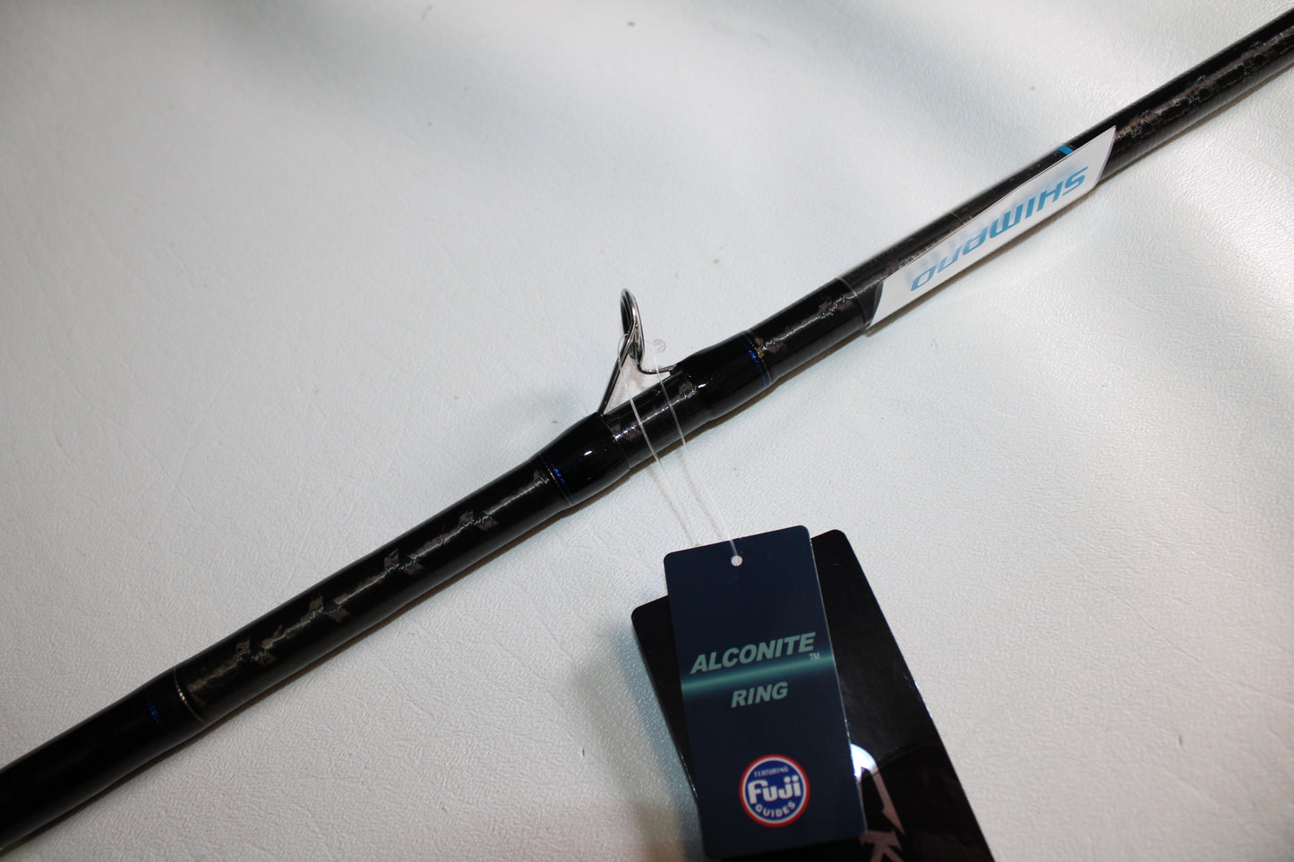A close-up of the Shimano SKIXX SKC86XH Used Casting Rod in mint condition, featuring the Shimano brand and an "Alconite Ring" tag by Fuji, displayed on a white surface.