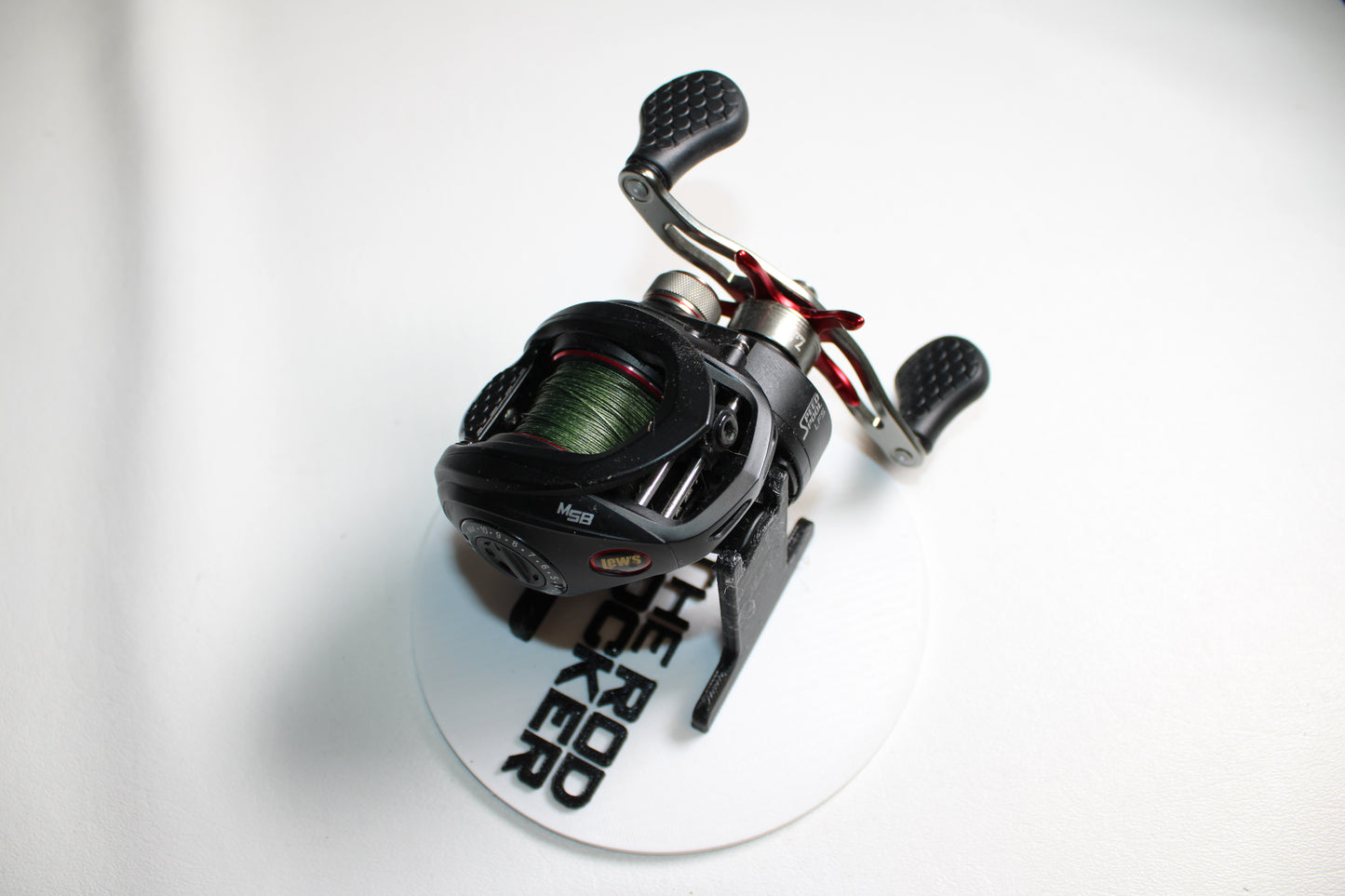 A Lew's Tournament MP TS1SHMPL 7.5:1 used casting reel in excellent condition, shown with green line on a white "THE ROD ROCKER" plate. Features dual textured handles. Upgrade with our Rod and Reel Trade-In Program for store credit!.
