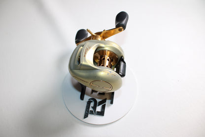 A Pflueger Trion LP 6.3:1 Gear Ratio Casting Reel in good used condition rests on a white circular surface with black letters, against a white background.