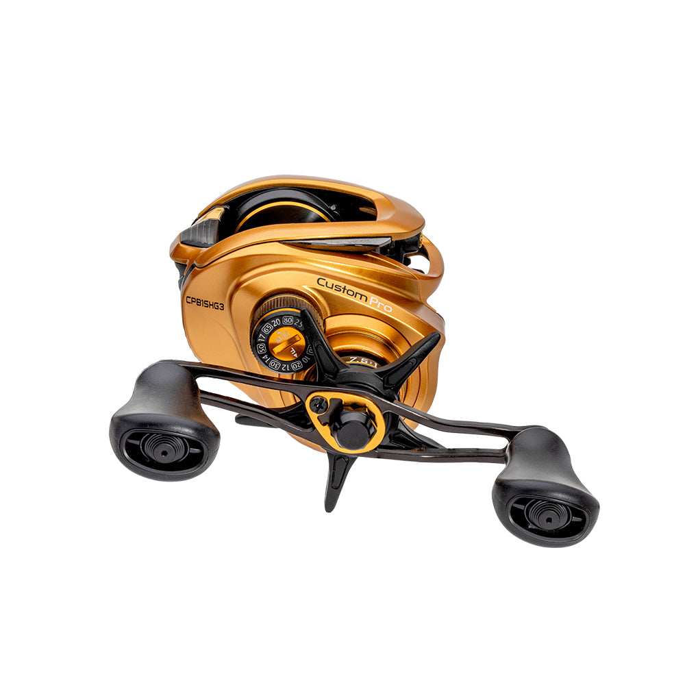 A Lew's Custom Pro Gen 3 Casting Reel 7.5:1 RH (CPB1SHG3) in gold and black with dual handles, adjustment dials, and Inertia Transfer Braking is displayed against a white background.