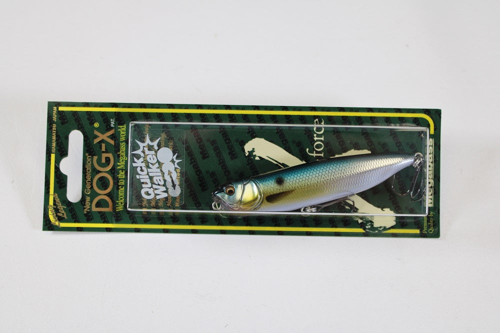 The Megabass Dog-X Quick Walker, by Megabass, is a packaged pencil bait with a shiny blue and yellow gradient back, silver sides, black eyes, and one-knock sound, displayed on green and black cardboard backing.