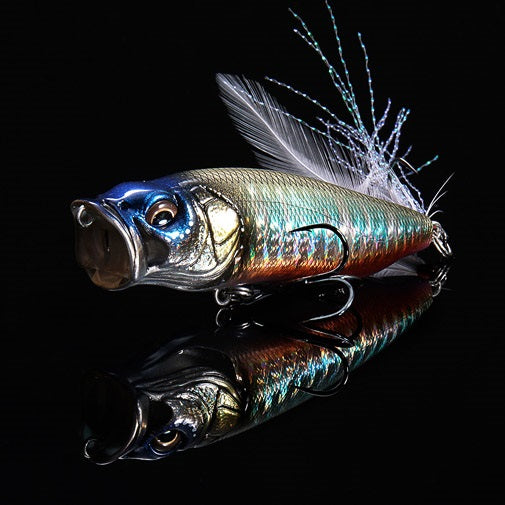 The Megabass PopMax (SP-C) Magome Oikawa fishing lure by Megabass features a lifelike fish shape, realistic details, and a feathered tail, displayed against a black reflective background.