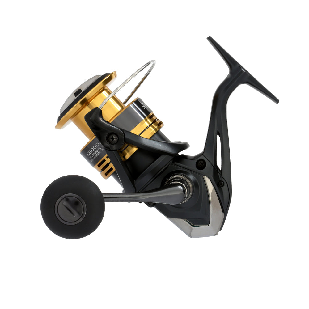 A close-up of the Shimano Sahara FJ Spinning Reel 5000XGFJ, featuring a sleek metallic black and gold finish, an ergonomic handle, and sturdy frame with HAGANE Gear for optimal angling performance.