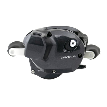 A close-up of the Shimano Tekota 300HGLCA 6.6:1 Line Counter Casting Reel shows its sleek black design, dual handles, and "Tekota" branding on the side. This compact Shimano reel is ideal for precise trolling and casting.