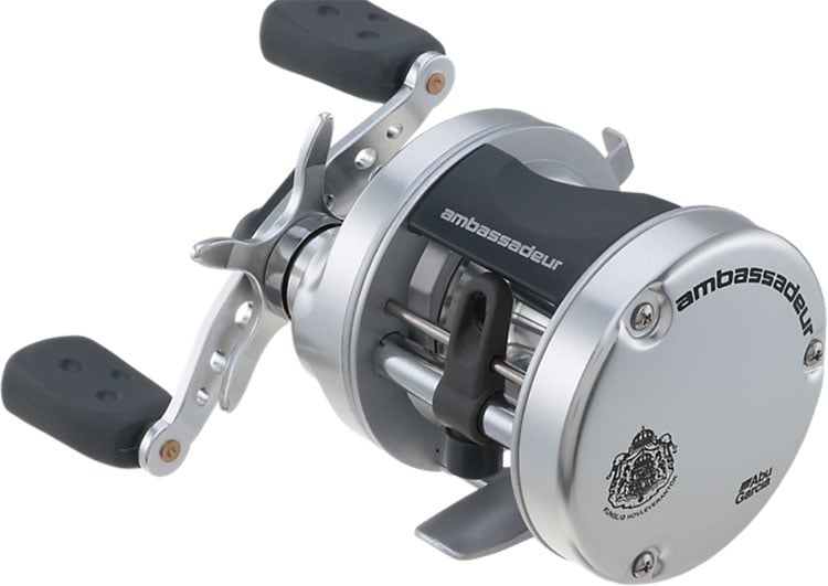 The Abu Garcia Ambassadeur S 5.1:1 Casting Reel 5500, in silver and black with dual handles, features "ambassadeur" and an emblem on its side. Its sleek cylindrical design with a metallic finish has an advanced centrifugal brake system for smooth operation.