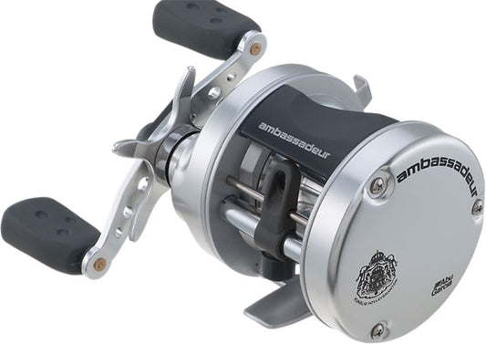The Abu Garcia Ambassadeur S 5.1:1 Casting Reel 5500, in silver and black with dual handles, features "ambassadeur" and an emblem on its side. Its sleek cylindrical design with a metallic finish has an advanced centrifugal brake system for smooth operation.