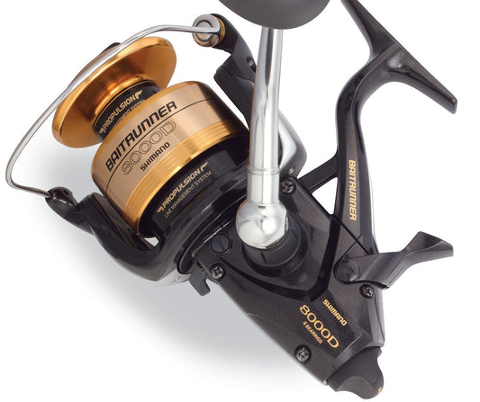 Close-up of a Shimano Baitrunner BTR8000D Spinning Fishing Reel, showing its gold and black design, Shimano branding, intricate parts, and the advanced Propulsion Line Management System.
