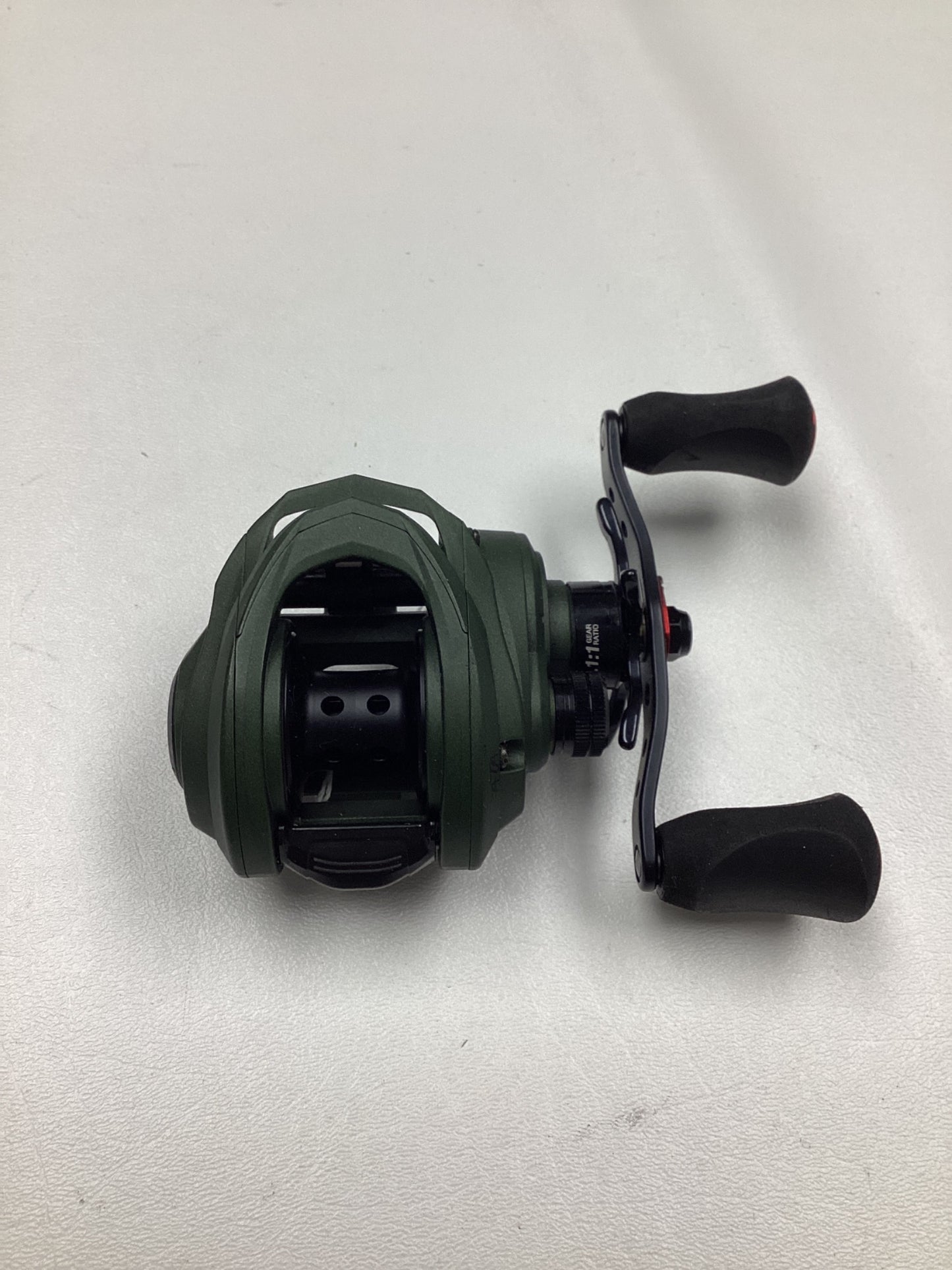 An Abu Garcia Zata 7.1:1 right-hand baitcasting reel in excellent used condition, featuring a green body, black handles, and a compact design, is displayed on a white surface.