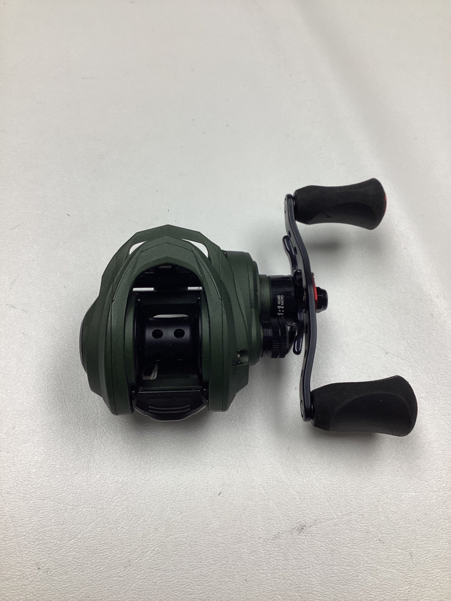 An Abu Garcia Zata 7.1:1 right-hand baitcasting reel in excellent used condition, featuring a green body, black handles, and a compact design, is displayed on a white surface.