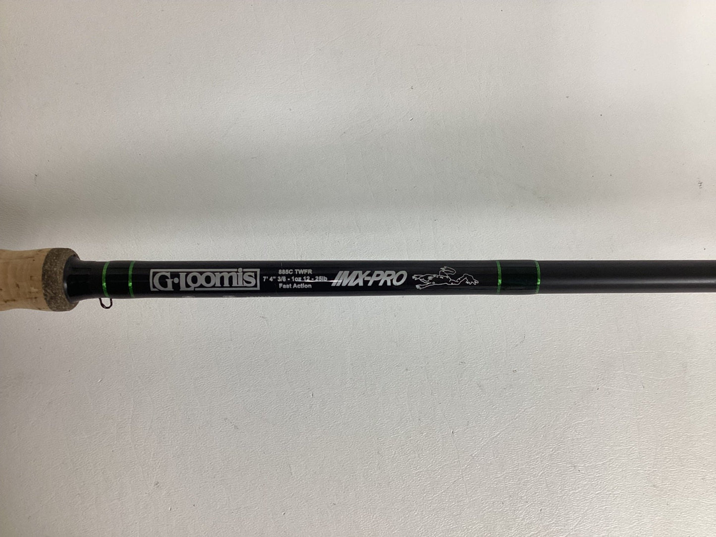 A close-up of a used G. Loomis IMX-PRO Frog Rod 885C TWFR 7'4" Mag Heavy Casting Rod in excellent condition, featuring the brand name, specs, logo on a black rod with green accents, and cork handle—ideal for your next trade-in.
