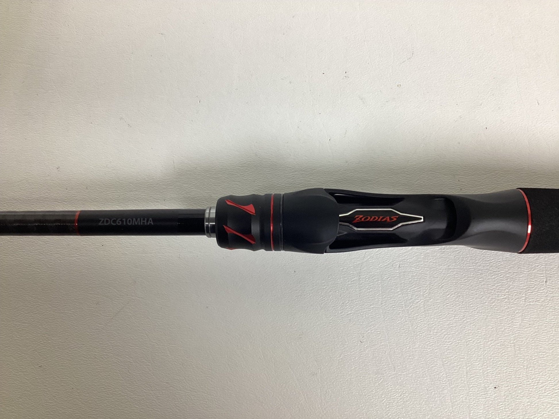 Close-up of a Shimano Zodias rod handle in black and red, ideal for the Nation's Best Rod and Reel Trade-In Program. The reel seat has red detailing with "Zodias" branding, while the rod section shows "ZDC610MHA" against a light background.