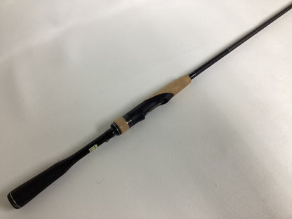 The Shimano Expride B EXS70LB, a used spinning rod in excellent condition, features a black handle with a light brown cork grip. Placed diagonally on a white surface, the black reel seat is visible as the rod extends out of frame.