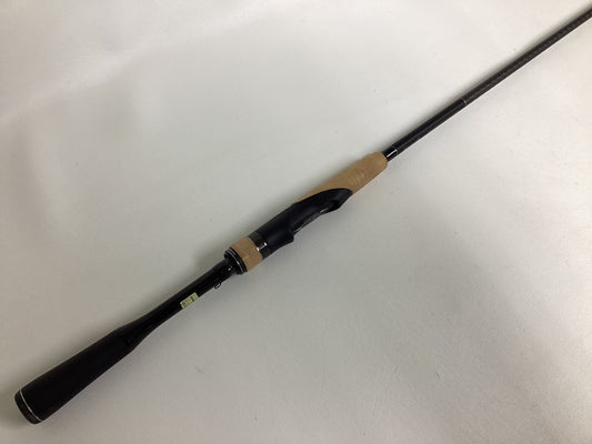 The Shimano Expride B EXS70LB, a used spinning rod in excellent condition, features a black handle with a light brown cork grip. Placed diagonally on a white surface, the black reel seat is visible as the rod extends out of frame.