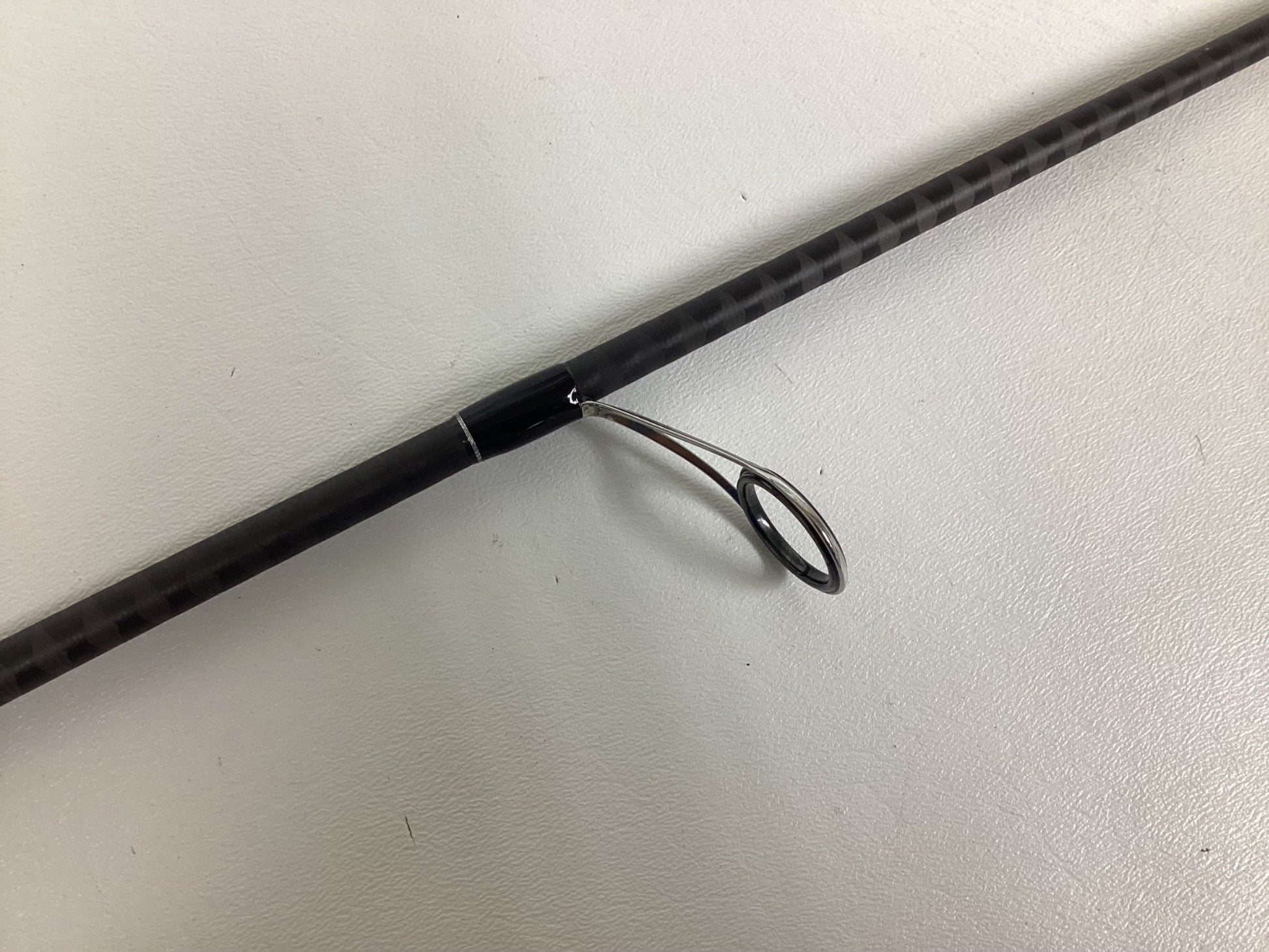 Close-up of the Shimano Expride B EXS70LB used spinning rod section showing a shiny metallic guide. The rod is dark and patterned, set against a plain white background, highlighting its excellent condition.