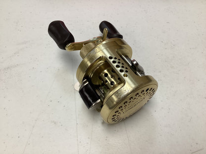 A Shimano Calcutta Conquest 101A 5.6:1 LH used casting reel in fair condition, gold-colored with two black handles and perforated metallic details, sits on a white speckled surface—great for quality gear or our Rod and Reel Trade-In Program.