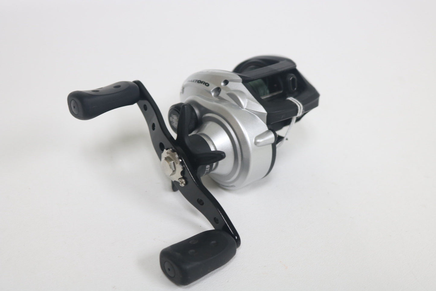 An Abu Garcia MAXTORO 5.3:1 casting reel in silver and black with dual handles, used in very good condition, displayed on a plain white background.