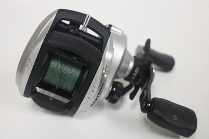 A close-up of an Abu Garcia MAXTORO 5.3:1 Casting Reel (Used - Very Good Condition) with green fishing line, silver and black body, and dual-handle grip, shown against a plain white background.