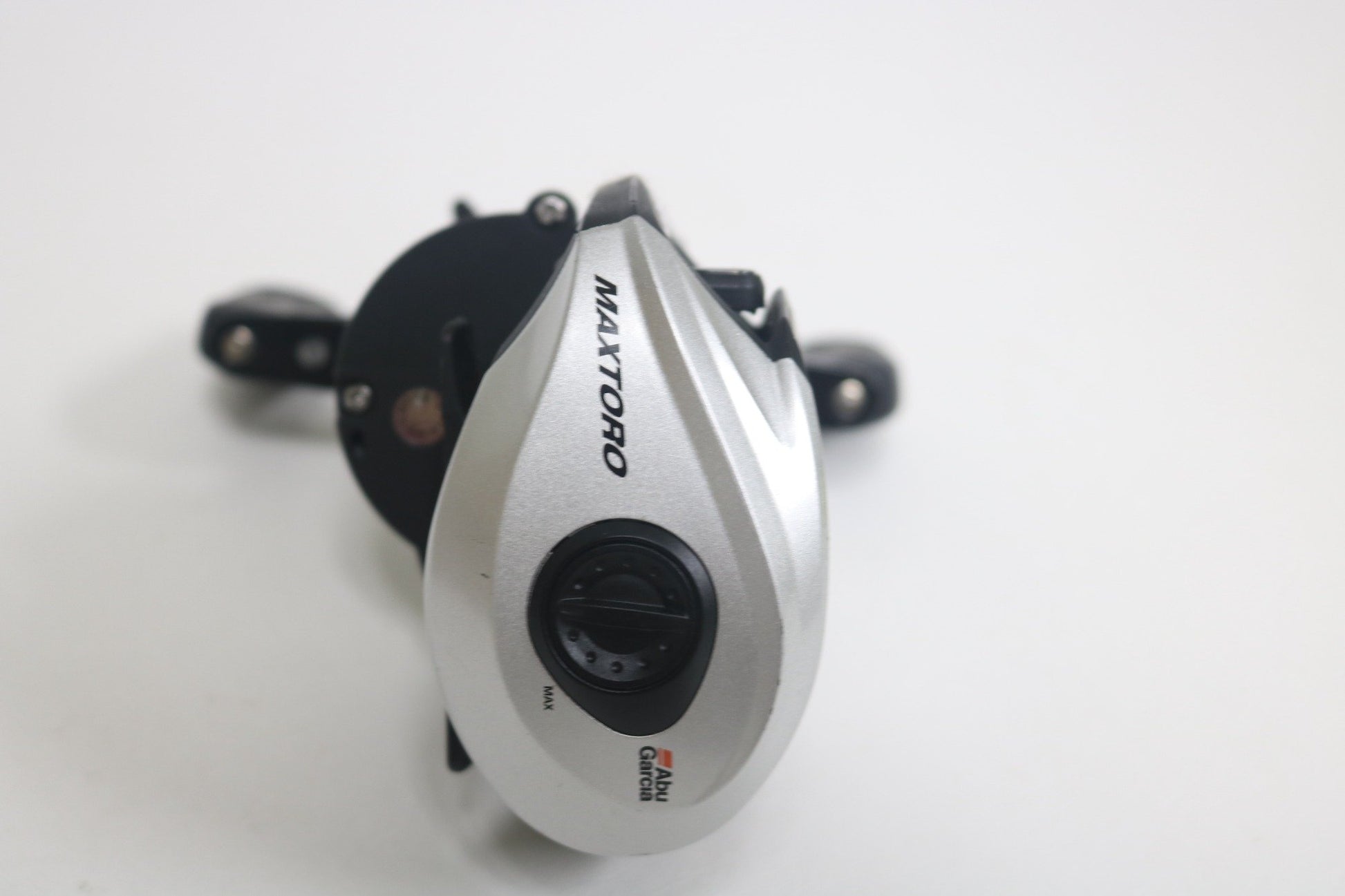 A silver and black Abu Garcia MAXTORO 5.3:1 baitcasting reel in very good used condition is shown on a white background, featuring an adjustment dial and the brand logo near the bottom.