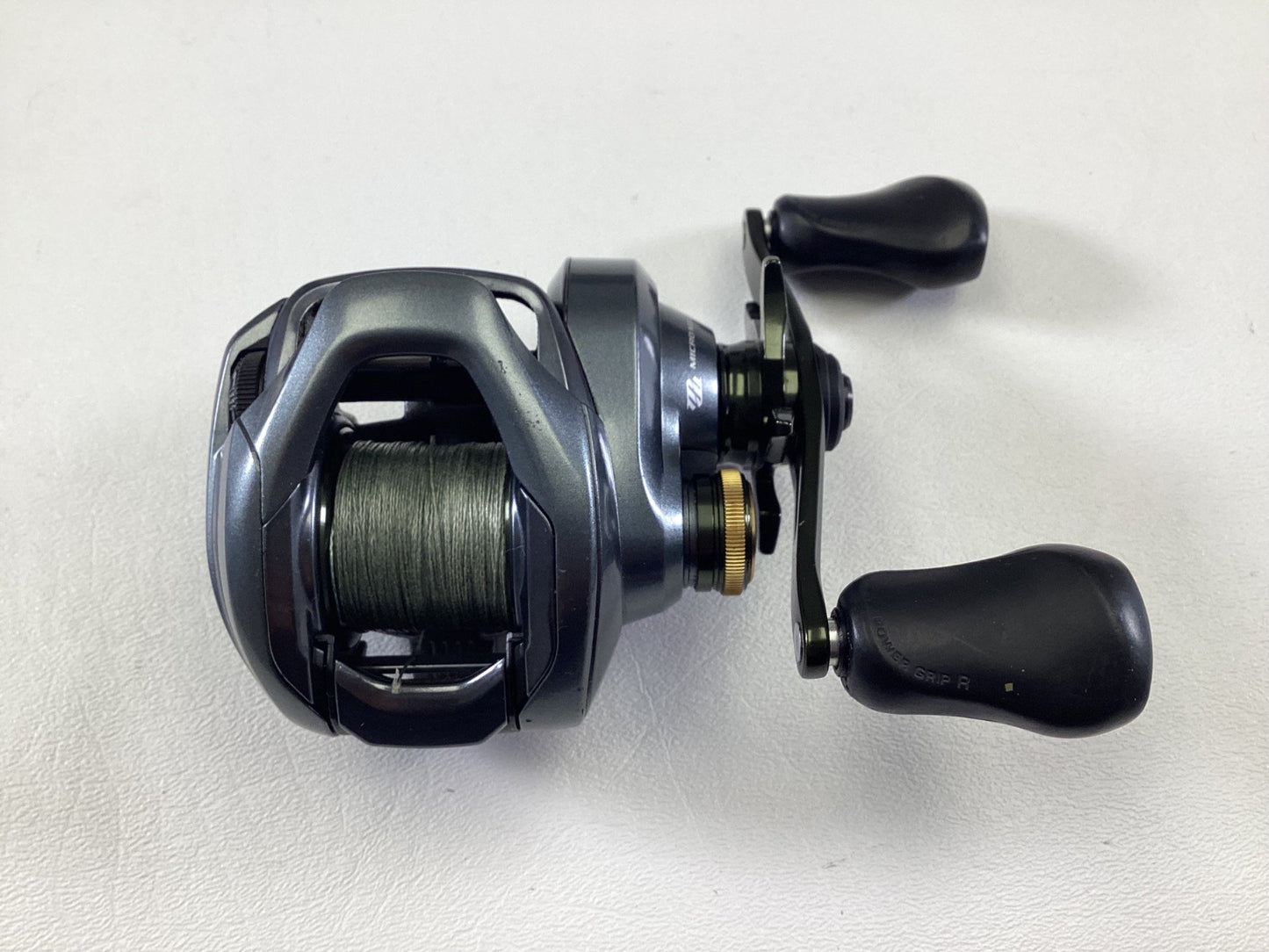 The Shimano Curado CUDC150XG Used Casting Reel, in very good condition, is displayed on a white surface. It features a metallic finish with a black handle and has its spool partially filled with green fishing line, exemplifying the quality associated with used Shimano gear.