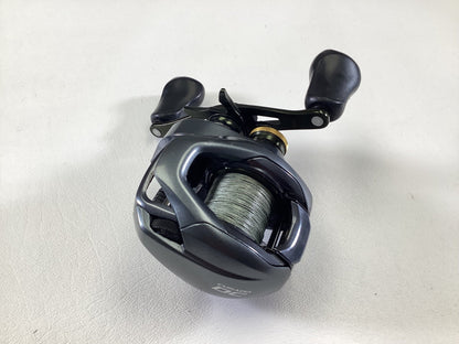 A Shimano Curado CUDC150XG used casting reel, featuring a sleek metallic finish with dual handles and dark-colored accents, is displayed on a light gray surface. This compact design is available through our Rod and Reel Trade-In program, providing anglers the opportunity to upgrade their gear while receiving store credit.
