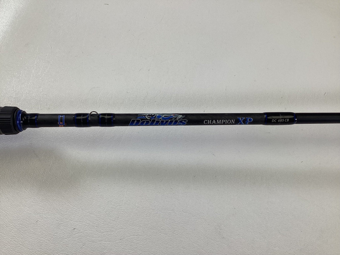 A close-up of a black Dobyns Champion XP DC685CB casting rod in excellent used condition, featuring blue and white lettering on a white background.