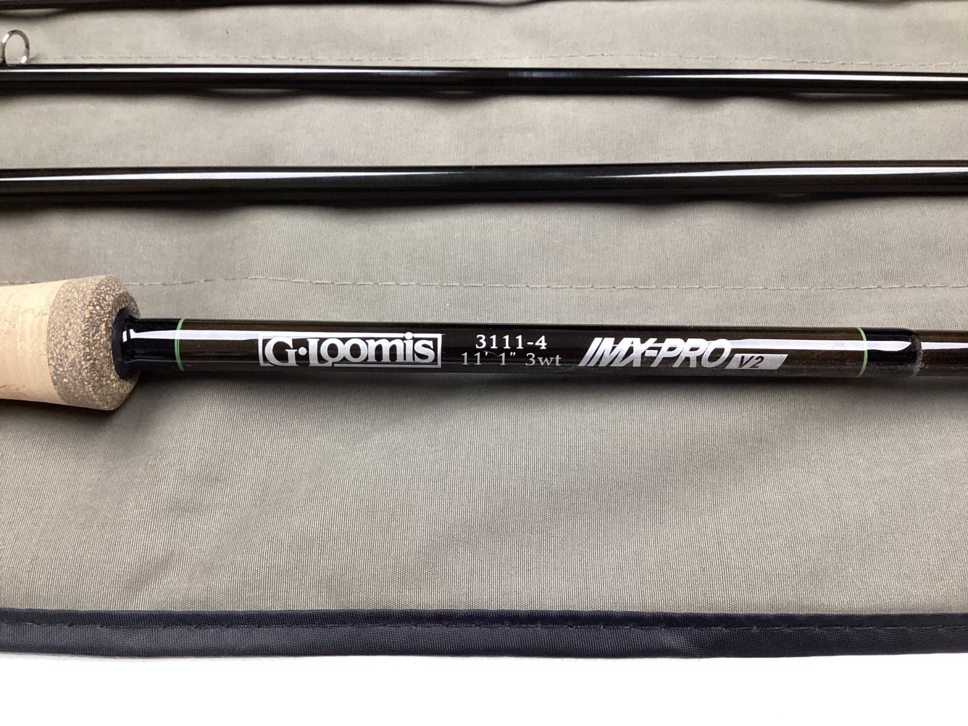 A close-up of a G. Loomis IMX-PRO V2 Shortspey 3111-4 11'1" #3 Used Fly Rod in mint condition with a cork handle, resting on its gray case—eligible for our rod and reel trade-in program for store credit.
