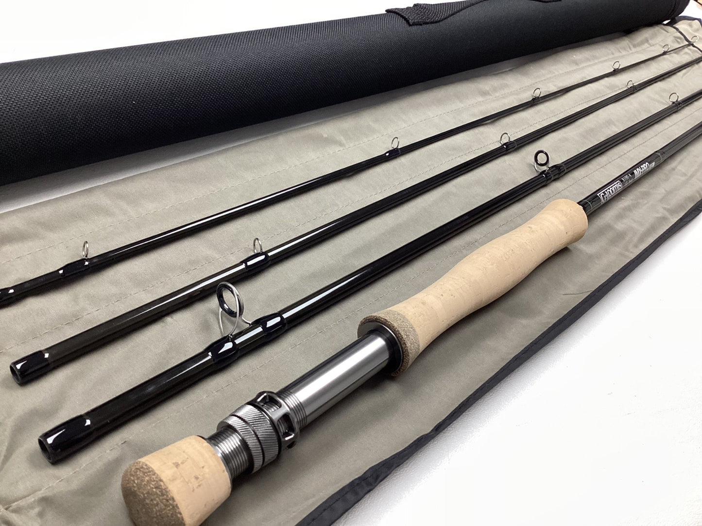 The G. Loomis IMX-PRO V2 Fly Rod 8100-4 10'0" #8, a used four-piece rod in mint condition with a cork handle and cloth case, is beside its black tube and eligible for our rod and reel trade-in program for store credit.