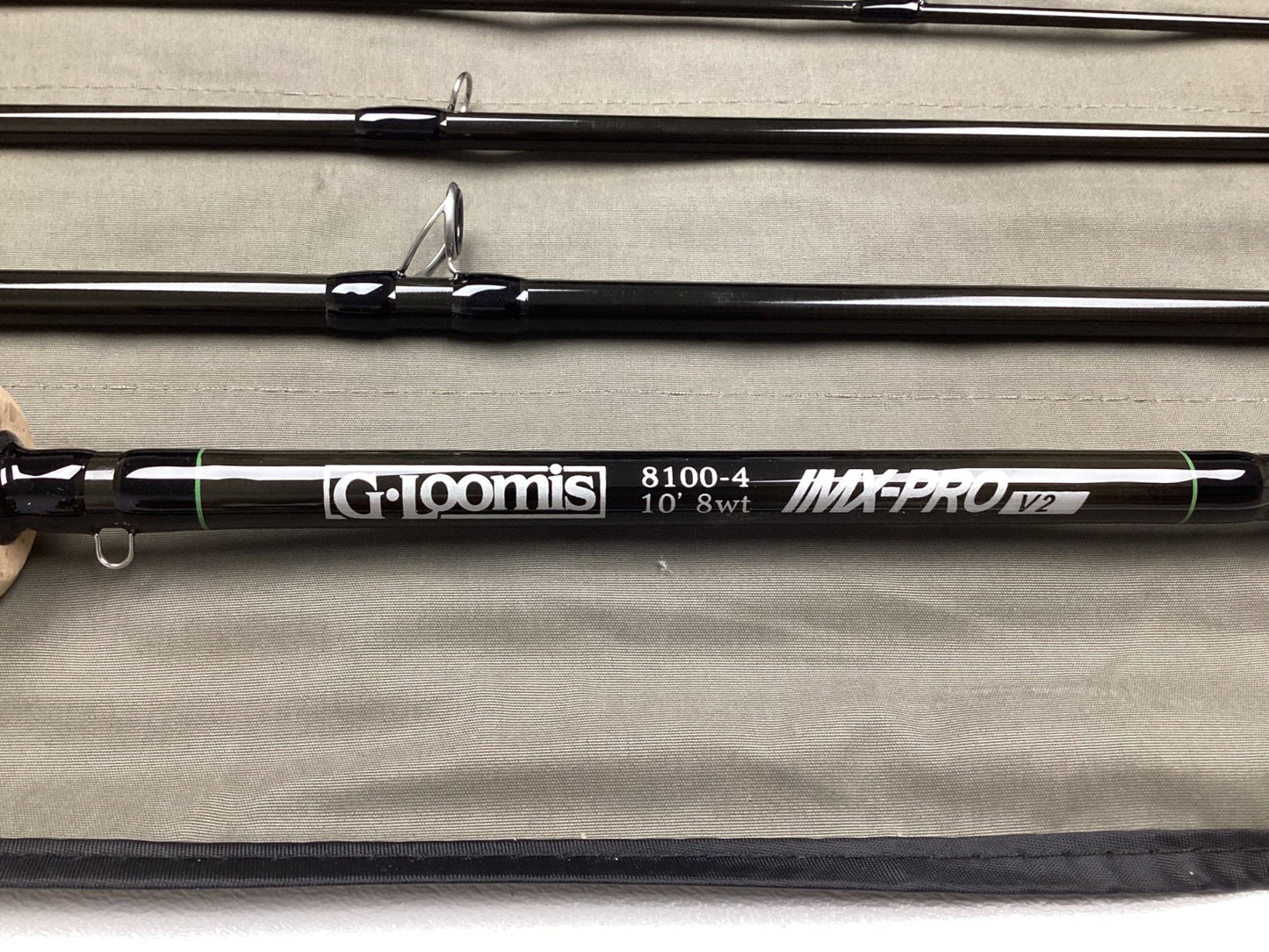 A G. Loomis IMX-PRO V2 Fly Rod 8100-4 10'0" #8, used but in mint condition, is displayed on khaki fabric with neatly aligned sections—perfect for anglers seeking quality from G. Loomis.