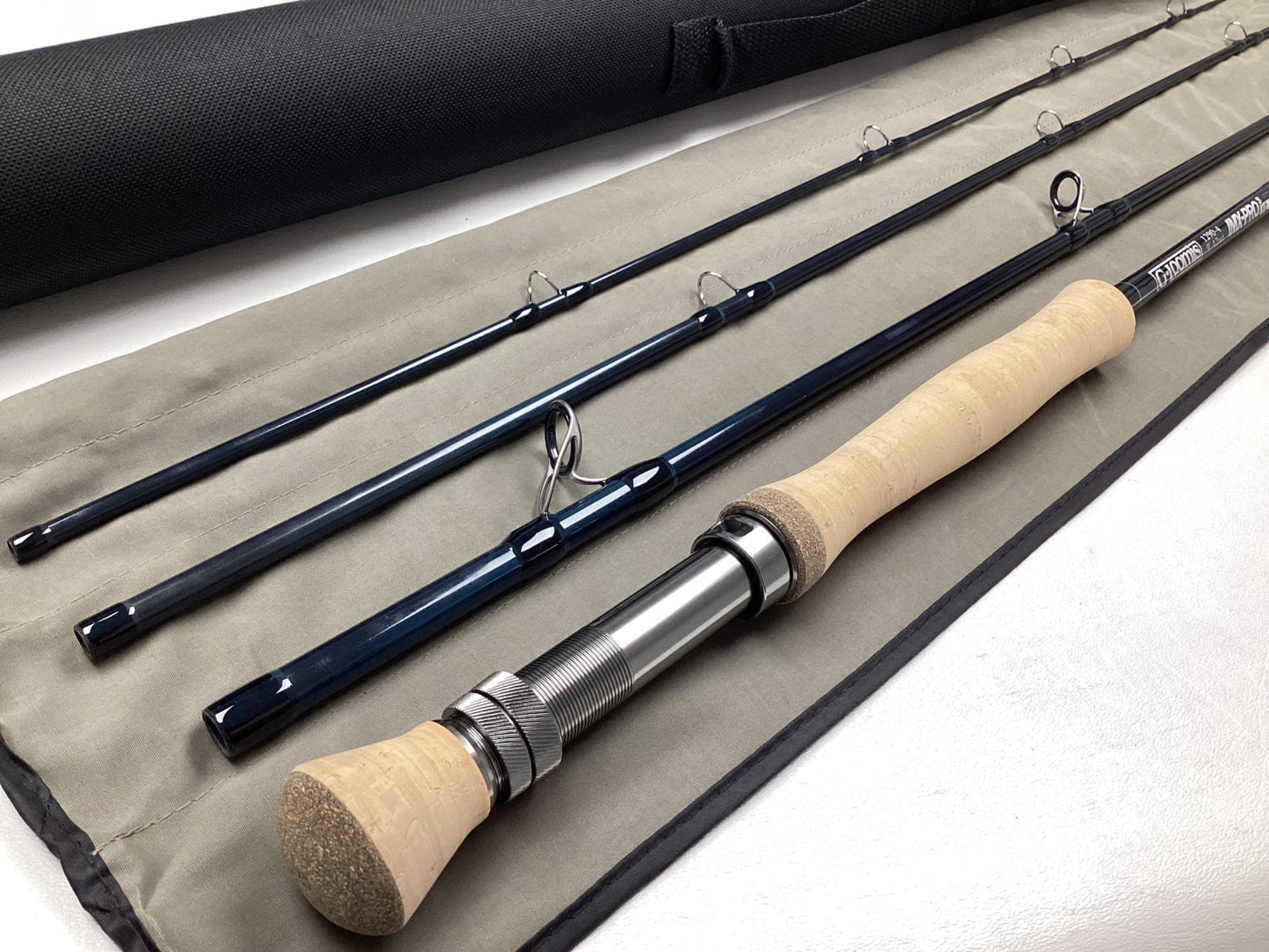The G. Loomis IMX-PRO V2S Saltwater 1290-4 9'0" #12 Used Fly Rod—Mint Condition—is displayed on its fabric case with a black carrying tube, ideal for those exploring our Rod and Reel Trade-In Program.