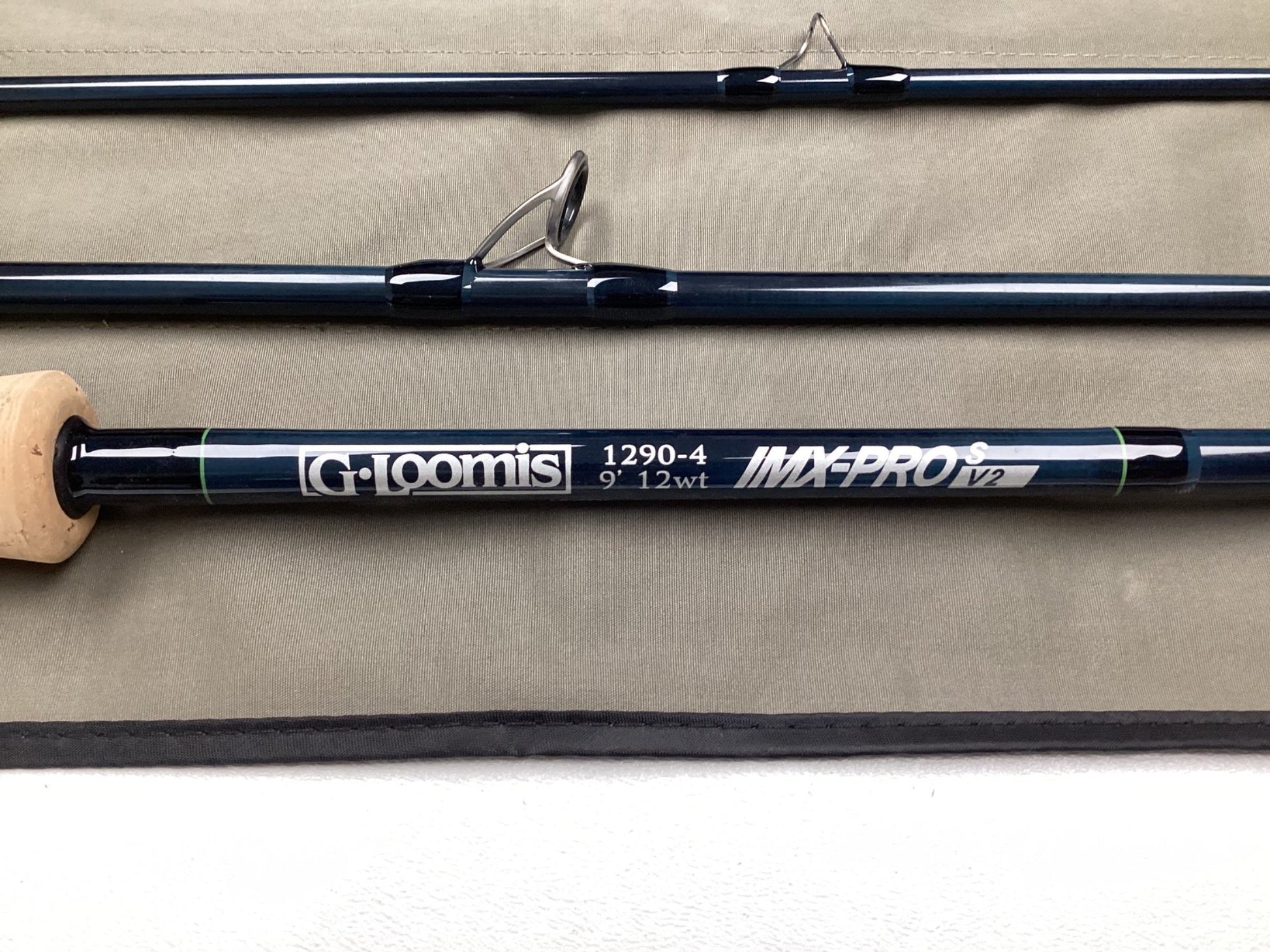 Three sections of the G. Loomis IMX-PRO V2S Saltwater 1290-4 9'0" #12 Used Fly Rod (mint condition) are displayed on gray fabric—ideal for those interested in our Rod and Reel Trade-In Program or quality pre-owned gear.