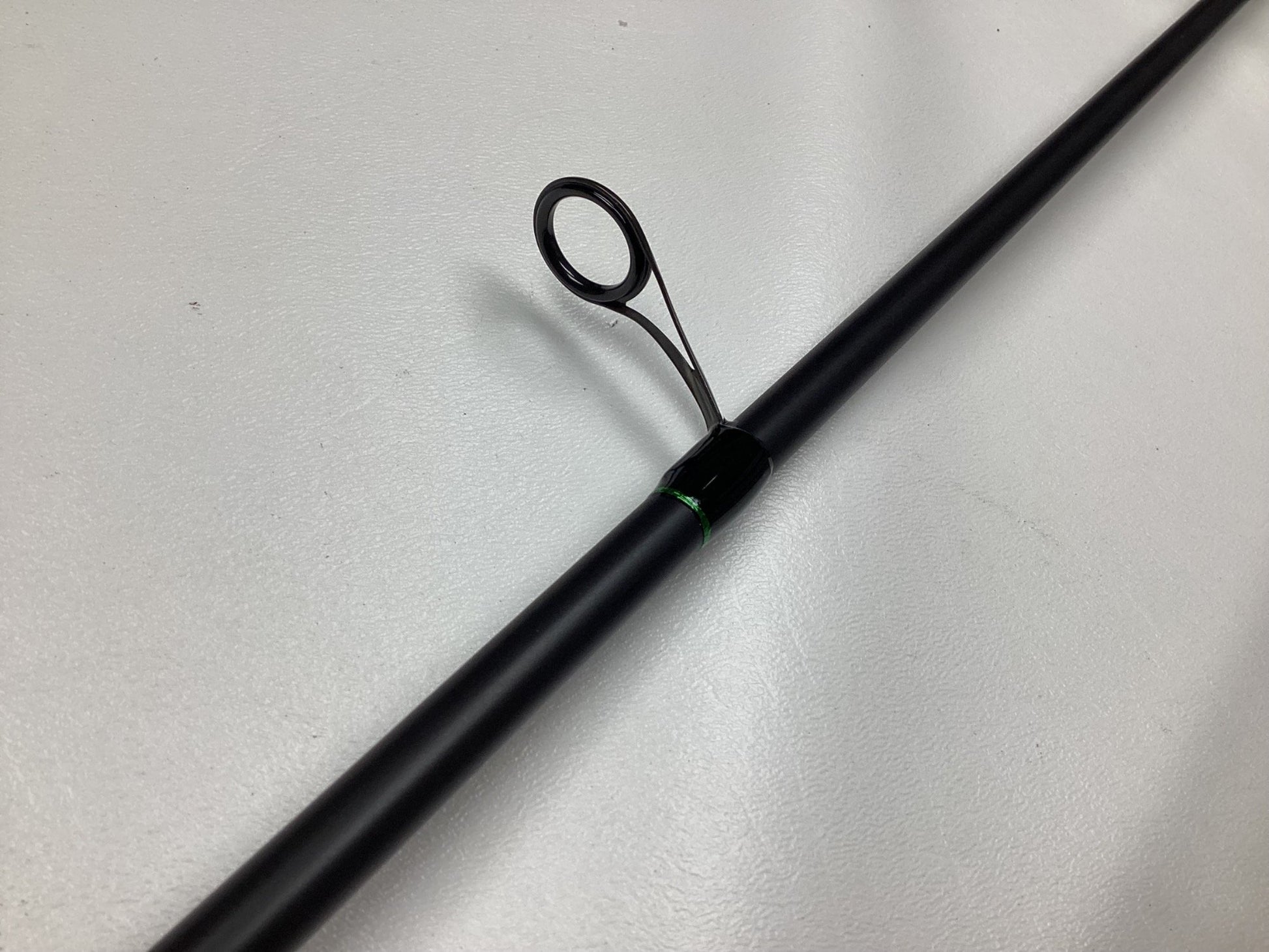 A close-up of the G. Loomis IMX-PRO Steelhead Centerpin Rod 1361-2CP STR 11'4" Medium Light (Used, Mint Condition), highlighting one of its line guides on a smooth, light-colored surface.