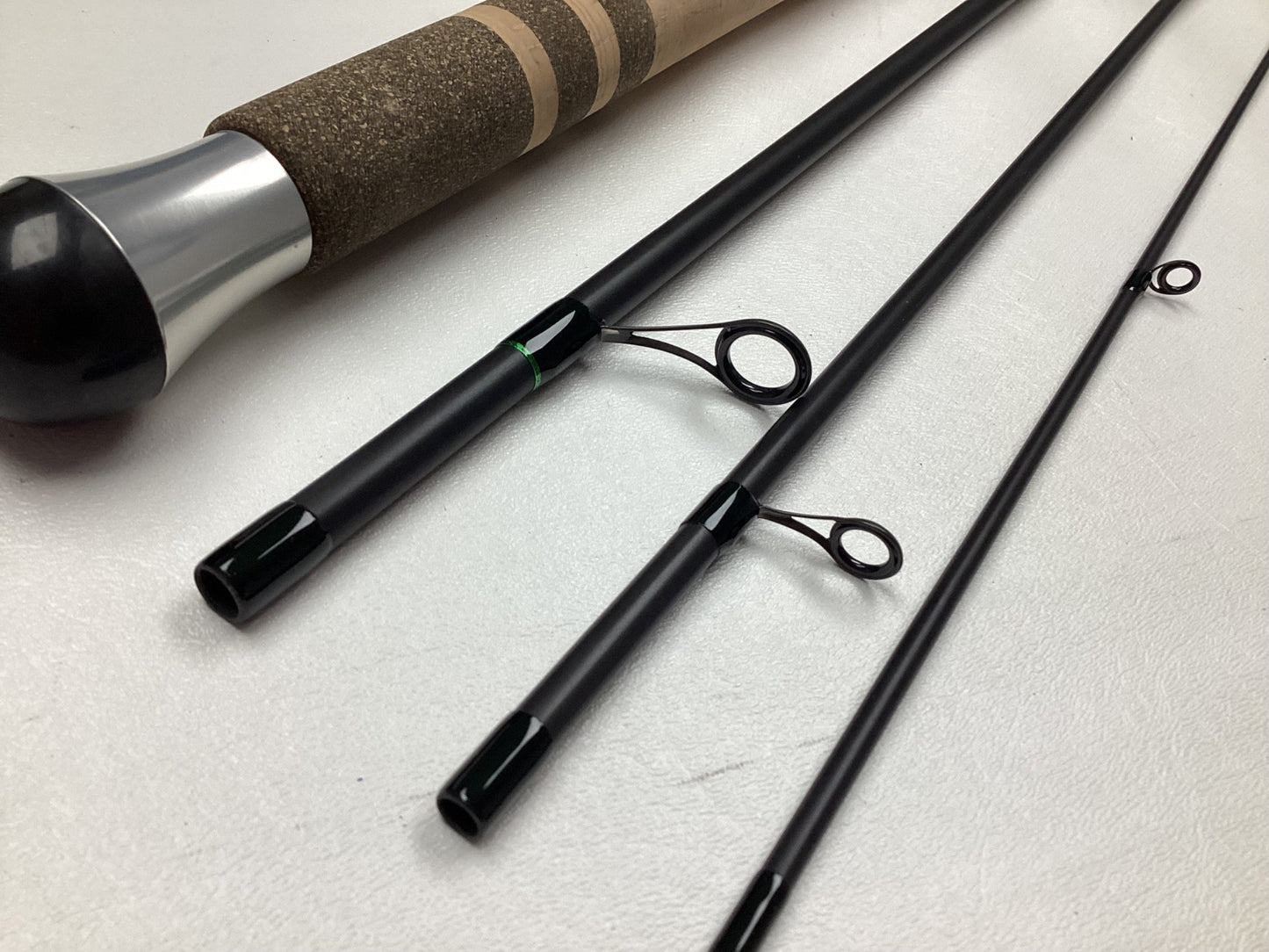 Close-up of a G. Loomis IMX-PRO Steelhead Centerpin Rod 13200-4CP STR 11'0" Ultra Light, used in mint condition, disassembled with cork handle, metal reel seat, and three rod sections with guides on a white surface.