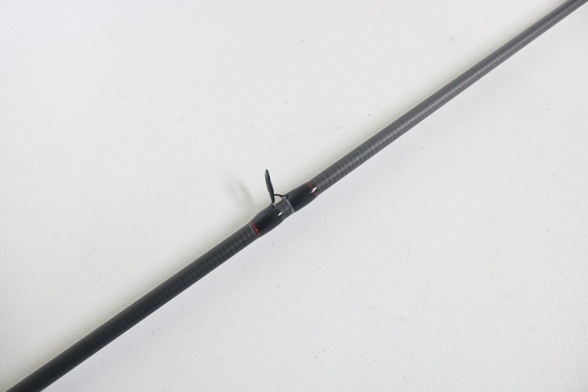 A Dobyns Kaden KD734CB 7'3" Medium Mod-Fast casting rod in excellent used condition rests diagonally on a white surface, featuring a carbon fiber build and a small black fin or propeller-like attachment at its center.