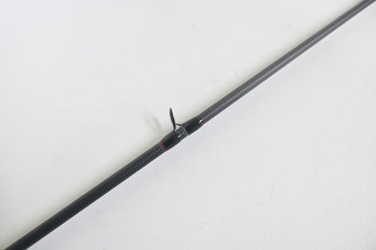 A Dobyns Kaden KD734CB 7'3" Medium Mod-Fast casting rod in excellent used condition rests diagonally on a white surface, featuring a carbon fiber build and a small black fin or propeller-like attachment at its center.