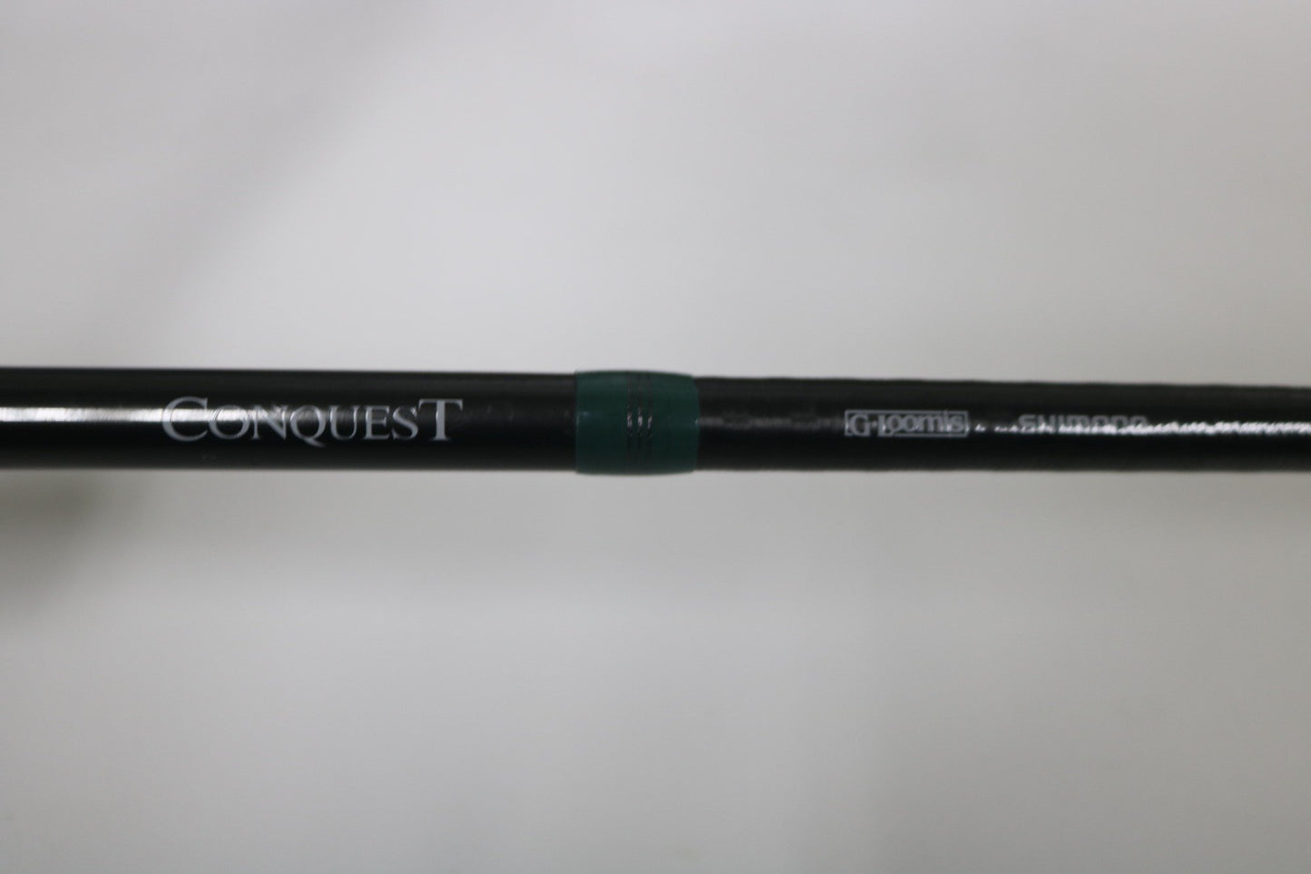 A close-up of a G. Loomis Conquest CNQ 904C MBR 7'6" Heavy Used Casting Rod in very good condition, with "Conquest" and "G. Loomis" printed on it and a green ring near the center. Ideal for our Rod and Reel Trade-In Program. Plain out-of-focus background.