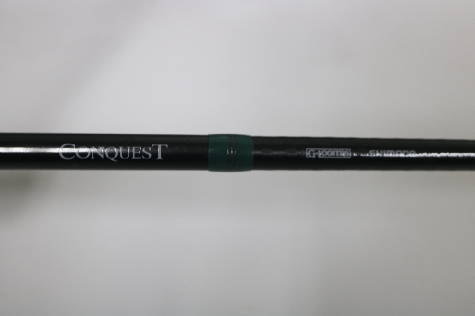 A close-up of a G. Loomis Conquest CNQ 904C MBR 7'6" Heavy Used Casting Rod in very good condition, with "Conquest" and "G. Loomis" printed on it and a green ring near the center. Ideal for our Rod and Reel Trade-In Program. Plain out-of-focus background.