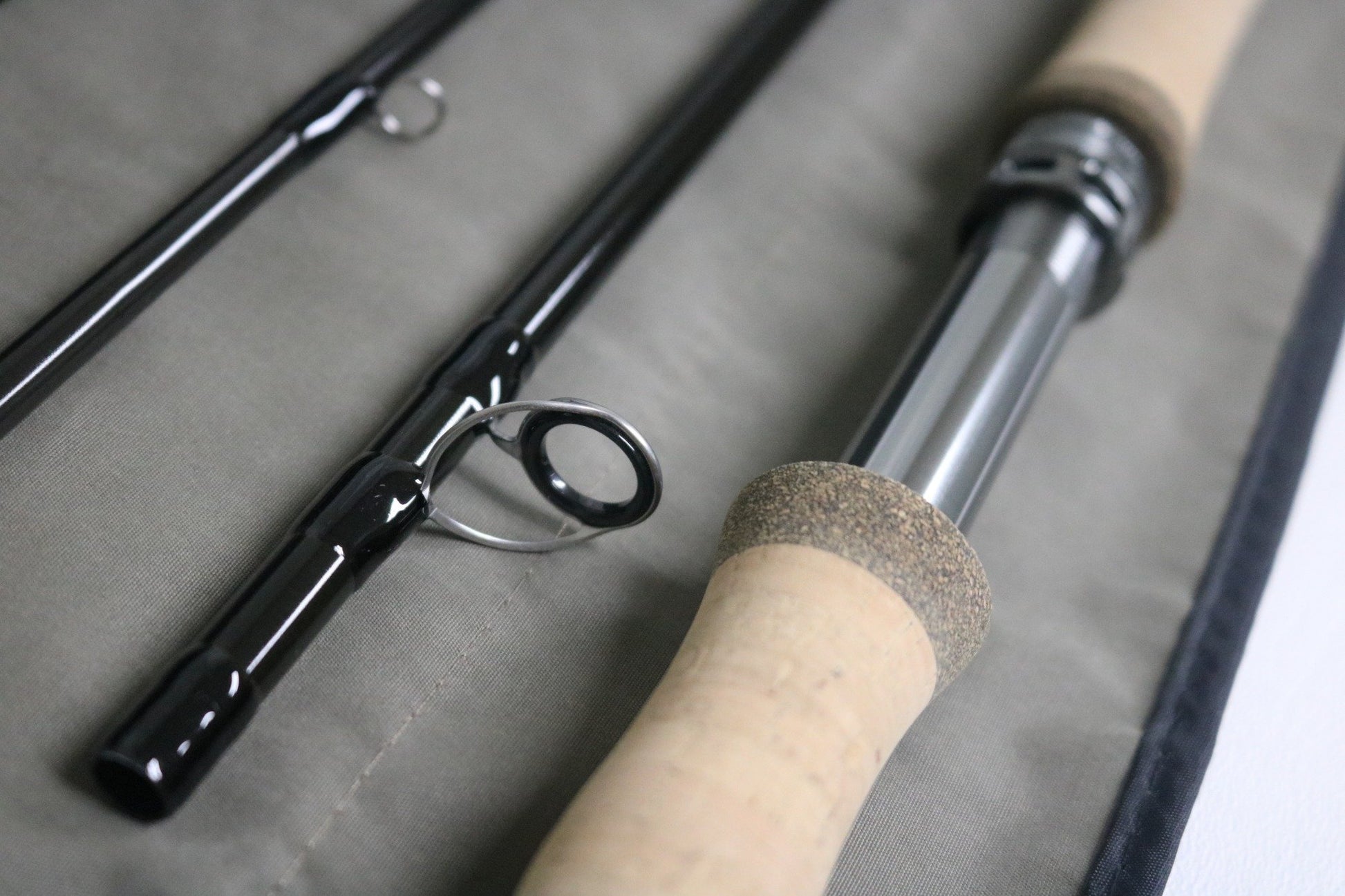 Close-up of a disassembled G. Loomis IMX-PRO V2 Shortspey 2111-4 11'1" #2 Used Fly Rod in mint condition with cork handle and metal reel seat on gray fabric. Trade your used gear for store credit with our Rod and Reel Trade-In Program!.