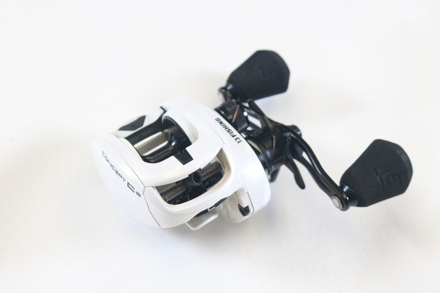 A white and black 13 Fishing Concept C2 C2-7.5-LH used casting reel with two black handles, in very good condition, placed on a white surface—ideal for our Rod and Reel Trade-In Program for store credit on used gear.
