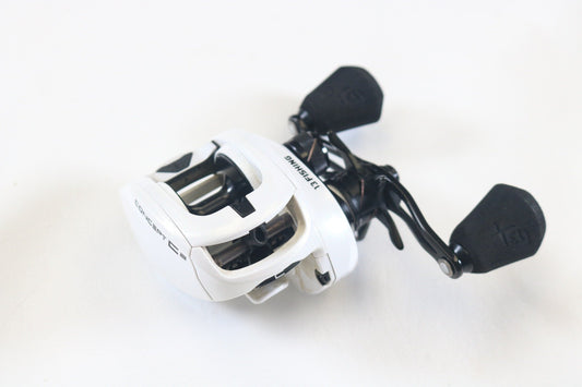 A white and black 13 Fishing Concept C2 C2-7.5-LH used casting reel with two black handles, in very good condition, placed on a white surface—ideal for our Rod and Reel Trade-In Program for store credit on used gear.