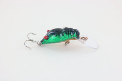 The WE Baits Red Eye Craw Green Foil is a green and black fishing lure with red eyes and two treble hooks from WE Baits, displayed on a plain white background.