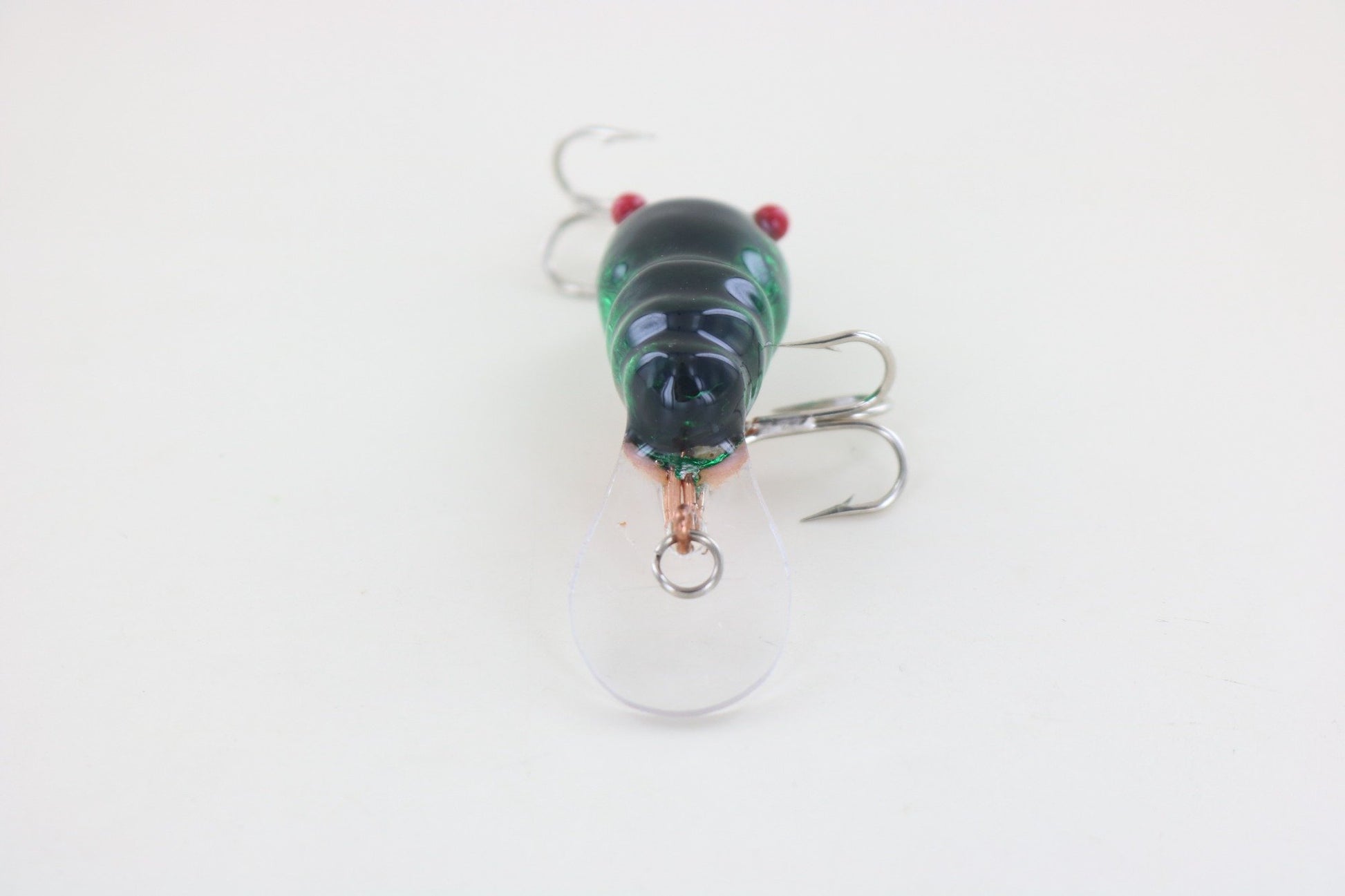 A close-up of the WE Baits Red Eye Craw Green Foil fishing lure by WE Baits, featuring a green and black finish, clear plastic lip, and treble hooks, displayed on a plain white background.