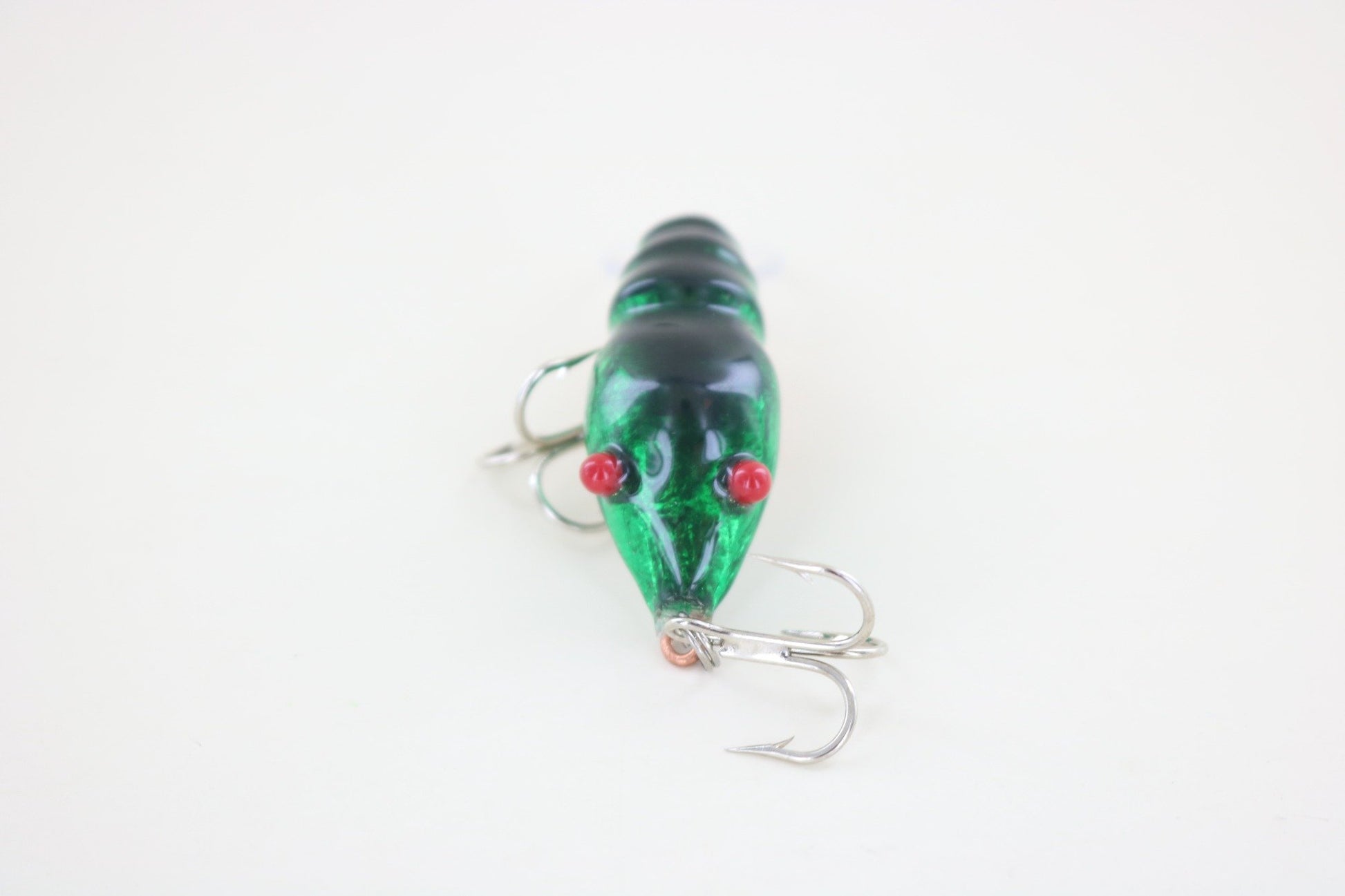 The WE Baits Red Eye Craw Green Foil by WE Baits, a green shrimp-shaped fishing lure with red eyes and two silver treble hooks, is shown on a plain white background.
