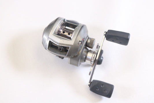 A used Abu Garcia Revo S Gen 1 6.4:1 LH casting reel in fair condition, with a silver finish and dual handle, sits on a white surface—ideal for upgrading through our rod and reel trade-in for store credit.