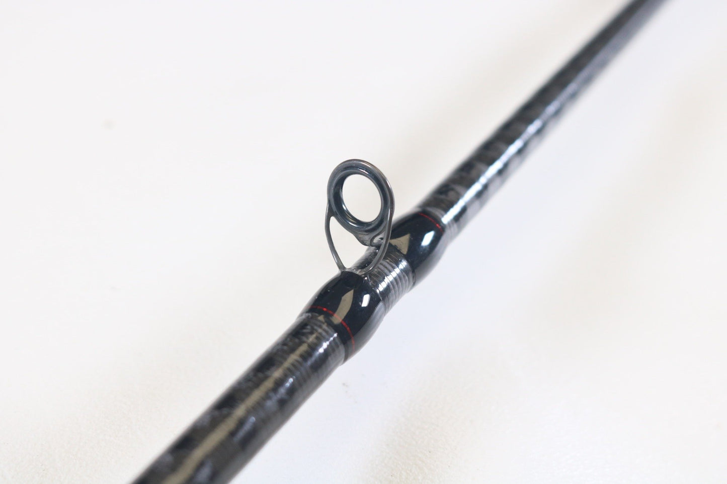 Close-up of the Shimano Zodias ZDC72MA 7'2" Medium casting rod in excellent condition on a white surface, highlighting a guide ring. The sleek black and silver design features a guide wrapped in black and red thread—ideal for those interested in our Rod and Reel Trade-In Program for store credit.