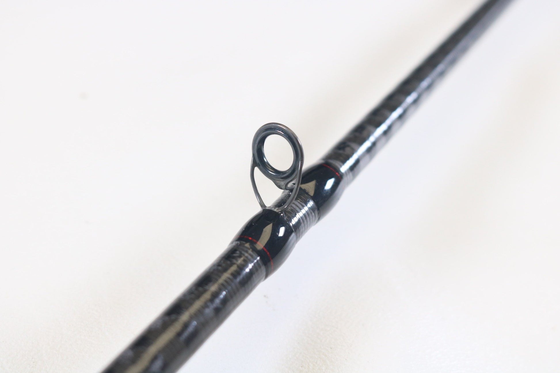 Close-up of the Shimano Zodias ZDC72MA 7'2" Medium casting rod in excellent condition on a white surface, highlighting a guide ring. The sleek black and silver design features a guide wrapped in black and red thread—ideal for those interested in our Rod and Reel Trade-In Program for store credit.