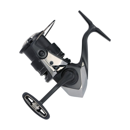 The Shimano Exsence B Spinning Reel C3000MHGB 5.8:1 by Shimano is shown from the side in sleek black and silver, featuring a large handle and advanced InfinityLoop technology for ultra-smooth casting against a white background.